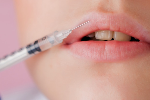 Doctor in gloves giving woman botox injections in lips, on pink background