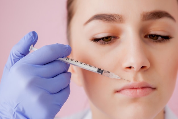 Doctor in gloves giving woman botox injections in lips, on pink space