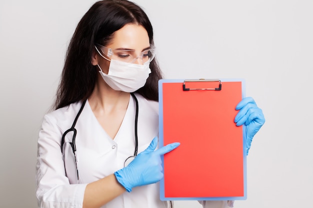 Doctor in a gloves, mask and glasses holds a blank form with space for text