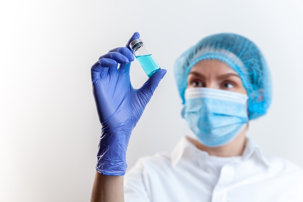 Doctor in gloves and mask holds bottle with vaccine medicine