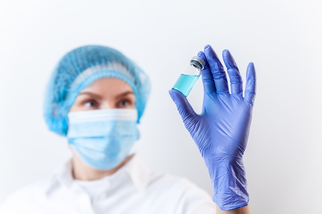 Doctor in gloves and mask holds bottle with vaccine medicine