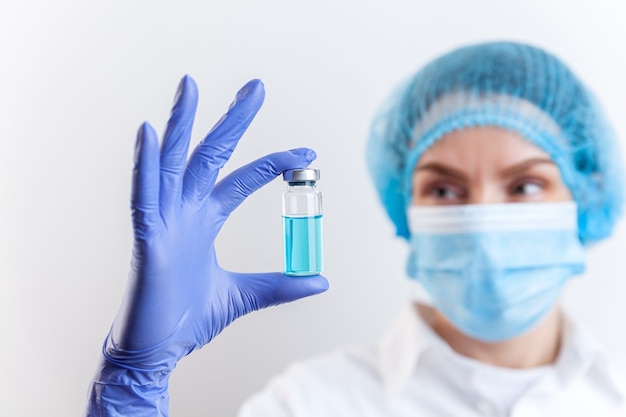 Doctor in gloves and mask holds bottle with vaccine medicine