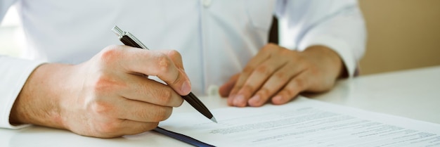 Doctor hand holding pen writing patient history list on note pad and talking to the patient about medication and treatment