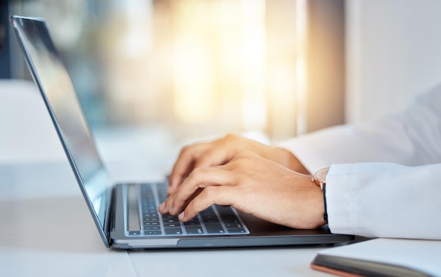 Doctor hands typing on a laptop doing medicine research at a hospital table and reading email online at work Healthcare expert or medical professional using keyboard and consulting via the internet