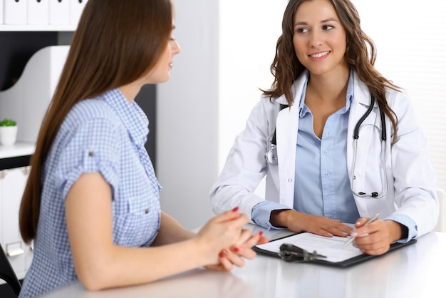 Doctor and happy patient talking while sitting at the desk. The physician or therapist discussing healthy lifestyle. Health care, medicine and patient service concept.