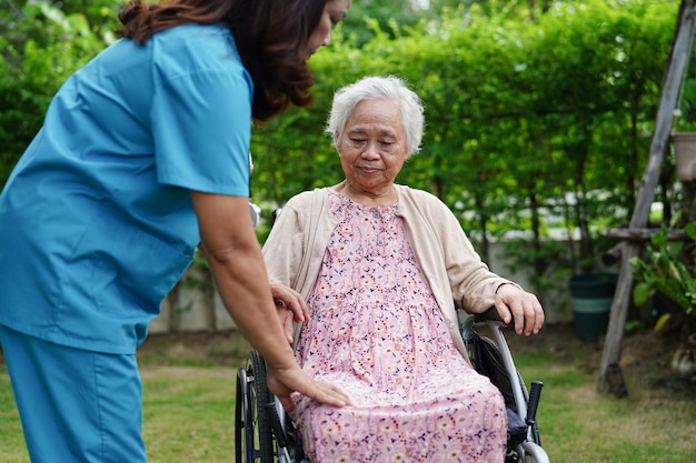 Doctor help Asian elderly woman disability patient sitting on wheelchair in park medical concept