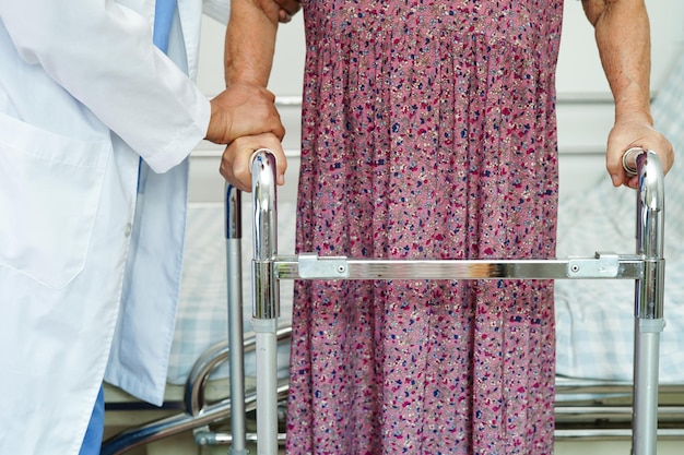 Doctor help Asian elderly woman disability patient walk with walker in nursing hospital medical concept