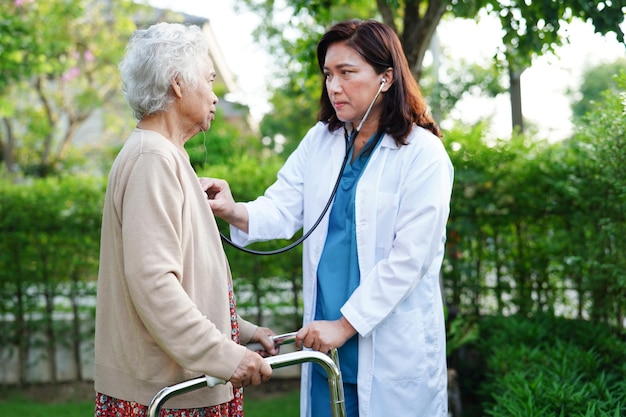 Doctor help Asian elderly woman disability patient walk with walker in park medical concept