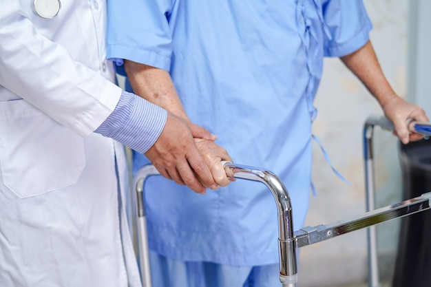 Doctor help Asian senior woman patient walk with walker at hospital.