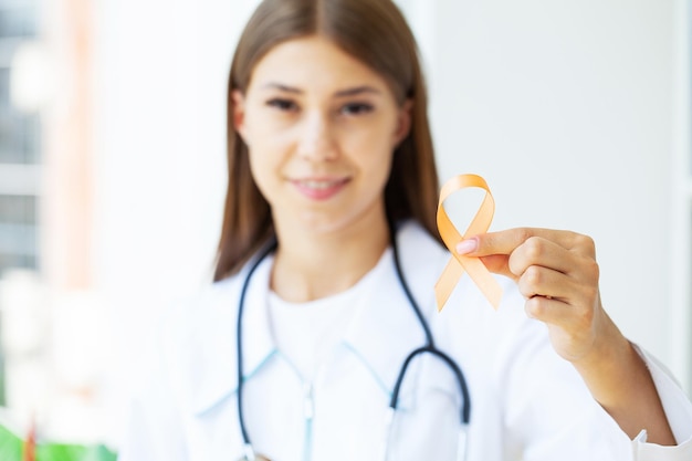 Doctor holding awareness orange ribbon standing in the clinic