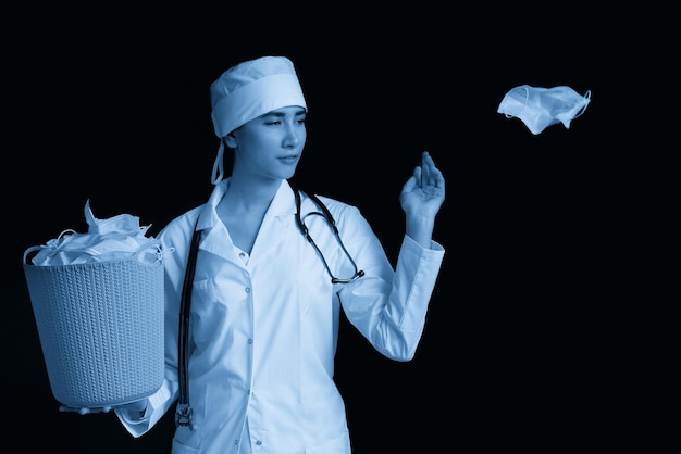 Doctor holding bucket full of used facial masks throwing them away as symbol of epidemic ending