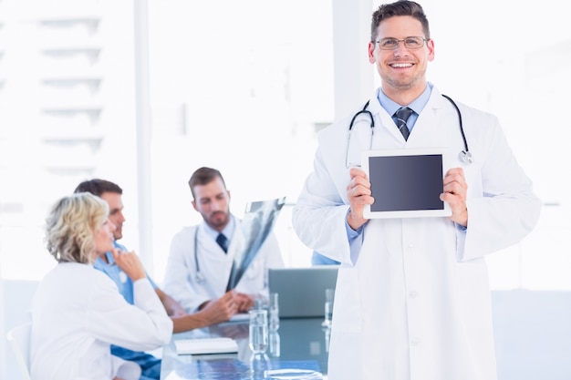 Doctor holding digital tablet with colleagues in meeting