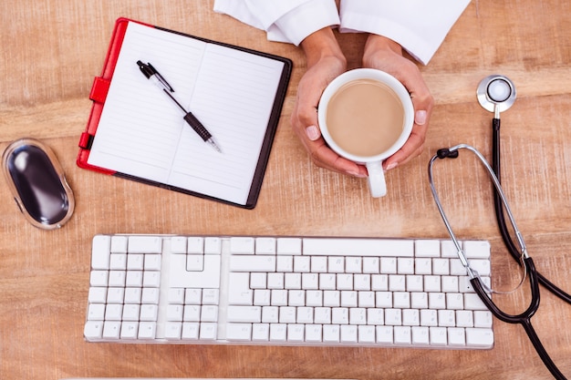 Doctor holding hot beverage on desk