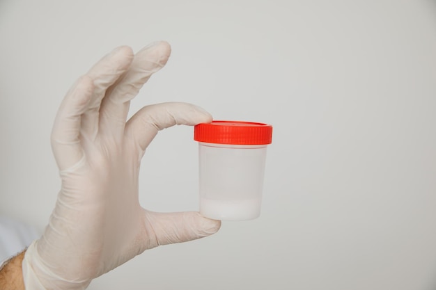 Doctor holding a plastic jar with sperm for semen analysis isolated on white. Medical test in hospital.