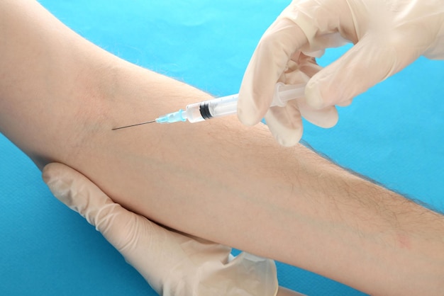 Doctor holding syringe with a vaccine in the patient hand on blue background