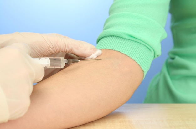 Doctor holding syringe with a vaccine in the patient hand on blue background