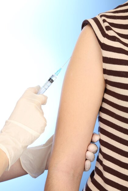 Doctor holding syringe with a vaccine in the patient shoulder on blue background