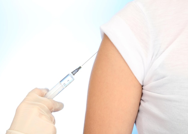 Doctor holding syringe with a vaccine in the patient shoulder on blue background