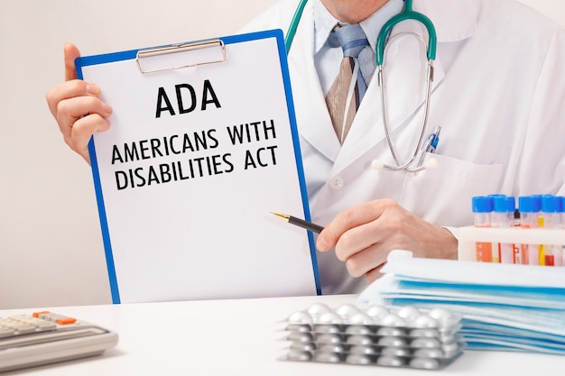 Doctor holds paper with American Disabilities ADA, stethoscope and pills on table