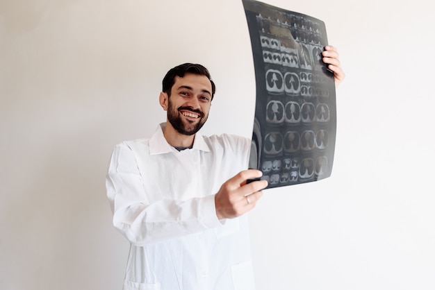 Doctor holds an x-ray in his hands and smiles on a white