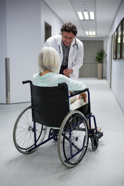 Doctor interacting with patient sitting on wheelchair in corridor