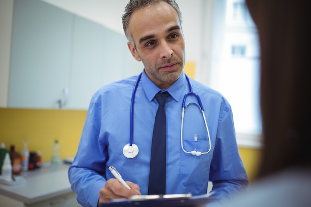 Doctor interacting with patient and writing on clipboard