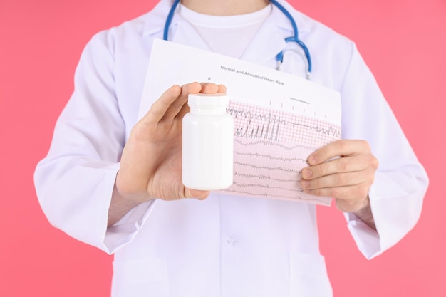 Doctor - intern holds cardiogram and bottle of pills on pink background