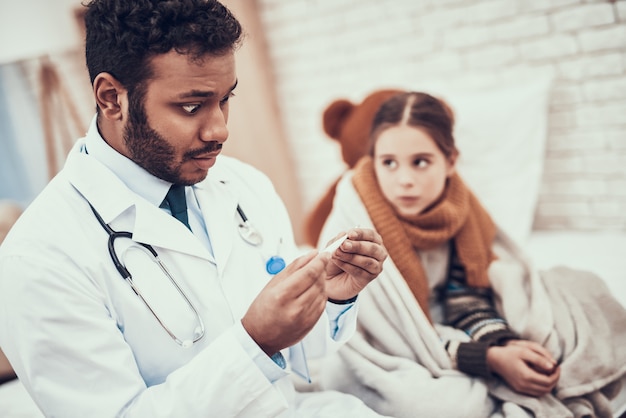 Doctor is taking temperature of little girl with cold.