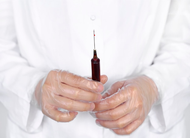 Doctor or lab scientist in personal protective equipment holding a syringe full of blood