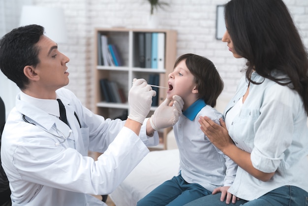 The doctor looks at the boy's throat.