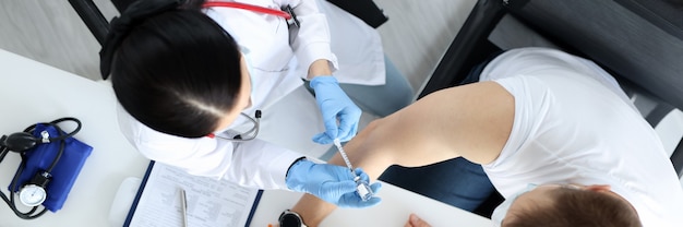 Doctor making injection of medicine into patients shoulder in laboratory top view vaccination