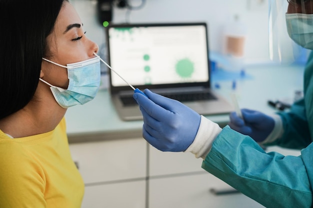 Doctor making nasal test to young woman in medical clinic for coronavirus infection - Focus on hand holding swab