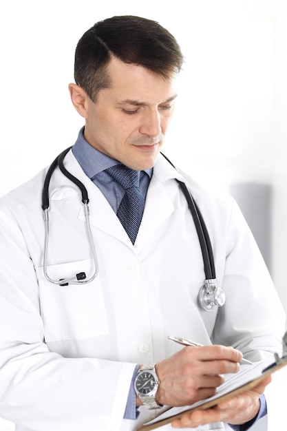 Doctor man using clipboard for filling up medication history records. Perfect medical service in clinic. Physician at work in hospital. Medicine and healthcare concepts.