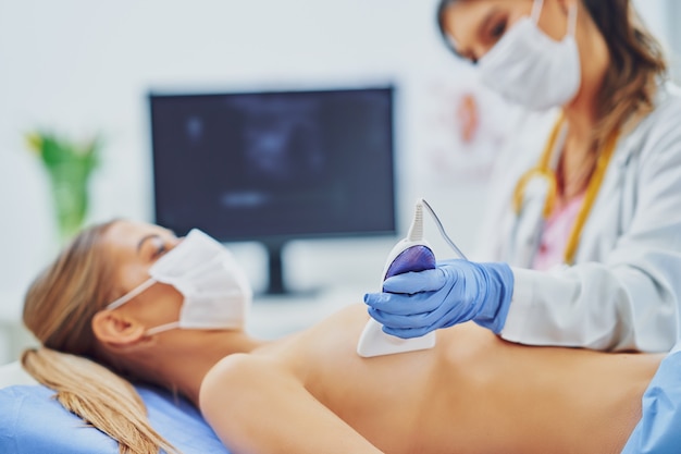 doctor in mask checking up breast to her patient