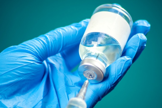 A doctor in medical gloves holding a bottle with vaccine and syringe before doing injection. Close up shot. Medicine and healthcare concept