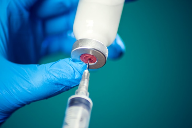 A doctor in medical gloves holding a bottle with vaccine and syringe before doing injection. Close up shot. Medicine and healthcare concept