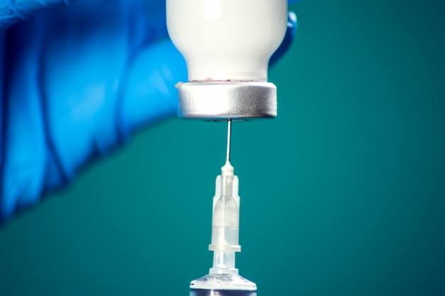 A doctor in medical gloves holding a bottle with vaccine and syringe before doing injection. Close up shot. Medicine and healthcare concept