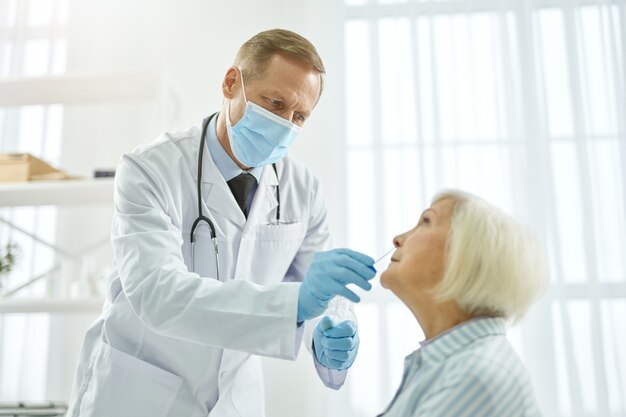 Doctor in medical mask doing covid nasal swab test for old woman