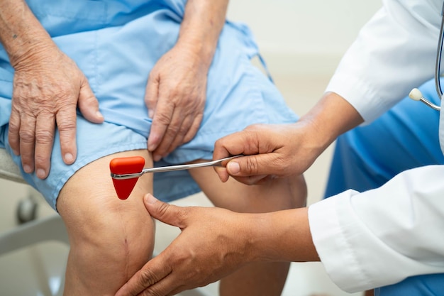 Photo doctor neurologist testing reflex knee with hammer and show asian senior scars surgical total knee joint replacement