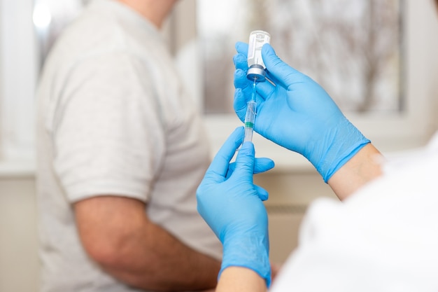 A doctor or nurse prepares to vaccinate a patient. Close-up - hands in blue gloves with a medical syringe inside a bottle of solution