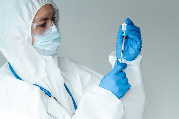 Doctor or nurse in a protective suit holds a syringe and a covid 19 vaccine