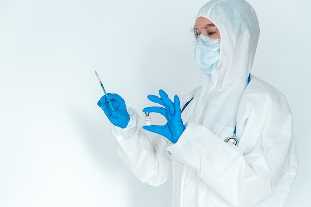 Doctor or nurse in a protective suit holds a syringe and covid 1