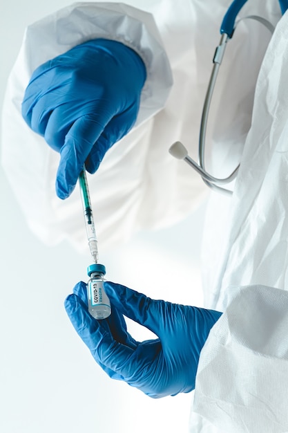 Doctor or nurse in a protective suit holds a syringe and covid 1