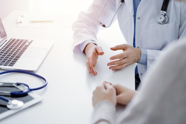 Doctor and patient discussing current health questions while sitting at the table in clinic office, only hands closeup. Medicine concept