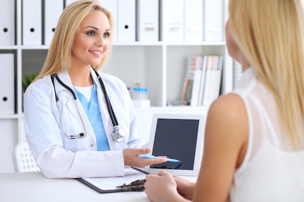 Doctor and patient discussing something while physician pointing into touch pad computer. Medicine and health care concept.