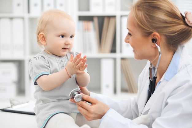 Doctor and patient in hospital. Little girl dressed in grey dress is being examined by doctor with stethoscope. Medicine concept.