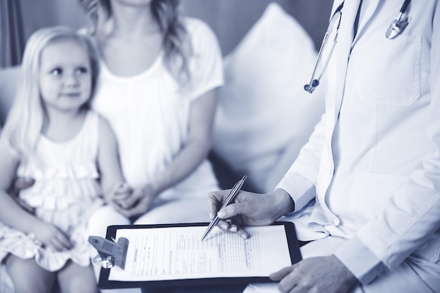 Doctor and patient. Pediatrician using clipboard while examining little girl with her mother at home. Happy cute caucasian child at medical exam. Medicine concept.