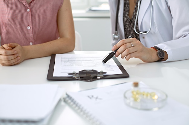 Doctor and patient sitting at the desk. Physician pointing into medical history records and explaining something to young woman. Medicine and health care concept.