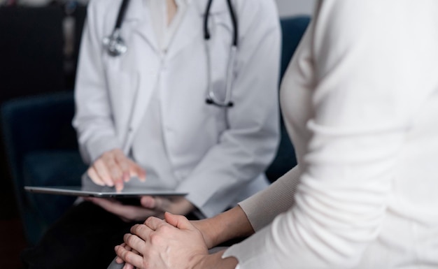 Doctor and patient sitting at sofa in clinic office. The focus is on female woman's hands, close up. Medicine concept