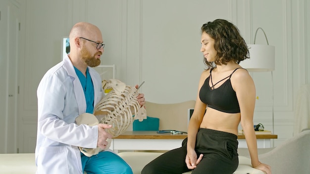 Doctor physiotherapist demonstrates the work of the spine to a young woman on a spine mockup healthc